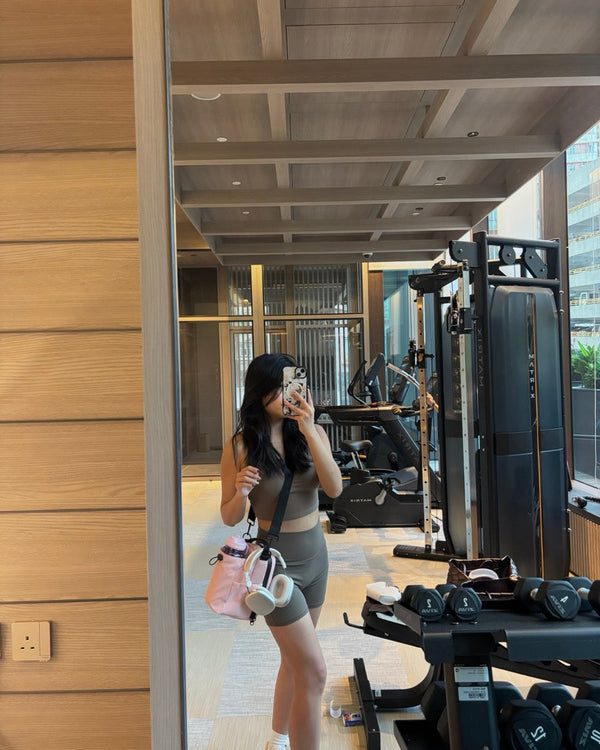 Woman taking a mirror selfie in a gym setting with exercise equipment and weights.