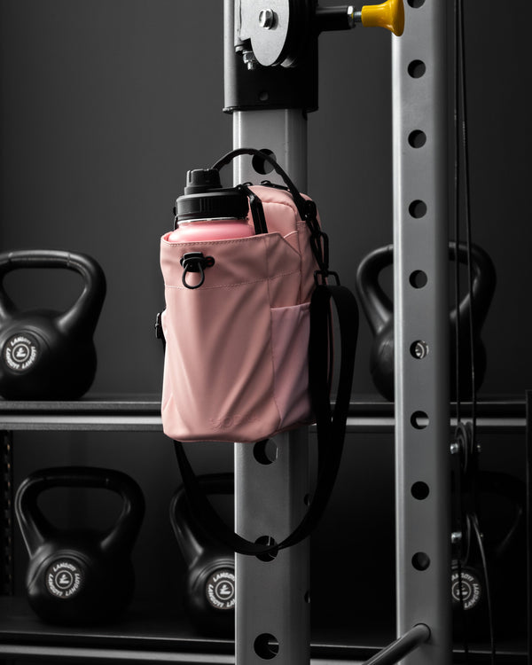 Pink water bottle holder attached to a gym squat rack with kettlebells in the background.
